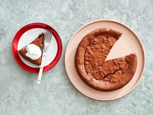 Slice of chocolate soufflé cake with whipped cream on a plate next to the entire cake.
